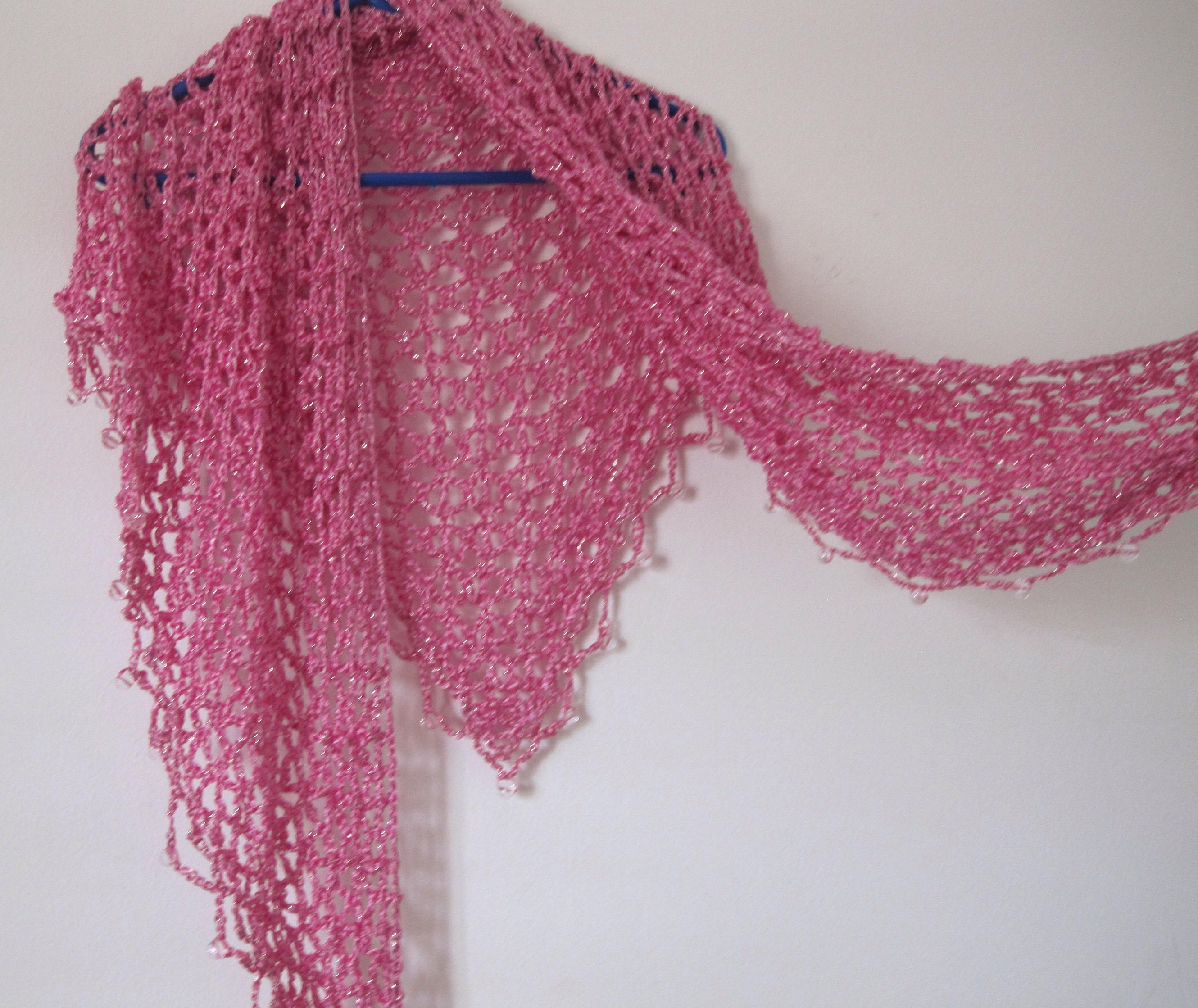 Blush pink shawl on a hanger, draped to show the openwork and beaded edge.